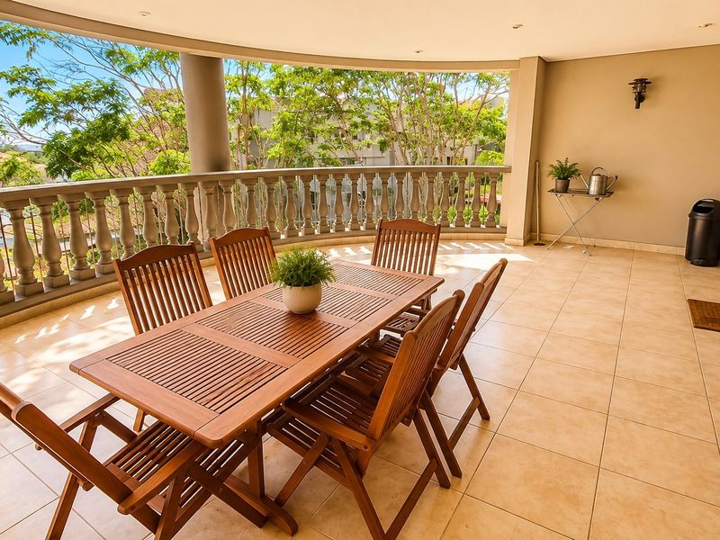 Spacious covered balcony featuring tiled flooring, a decorative balustrade, and recessed lighting, offering a pleasant outdoor area for relaxation and dining.