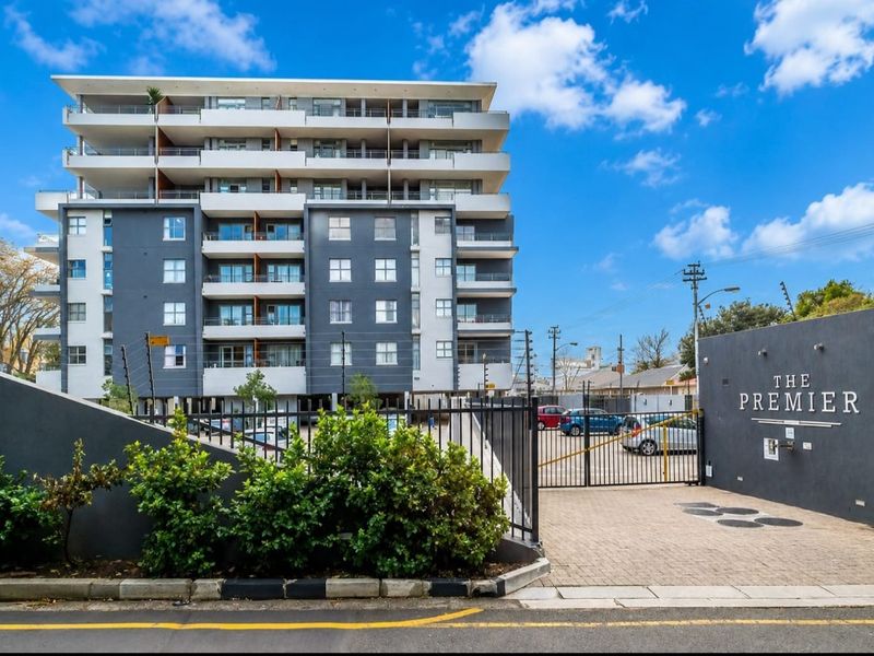 Front exterior view of The Premier apartment complex, featuring modern architecture, secure gated access, paved driveway, and multiple balconies.