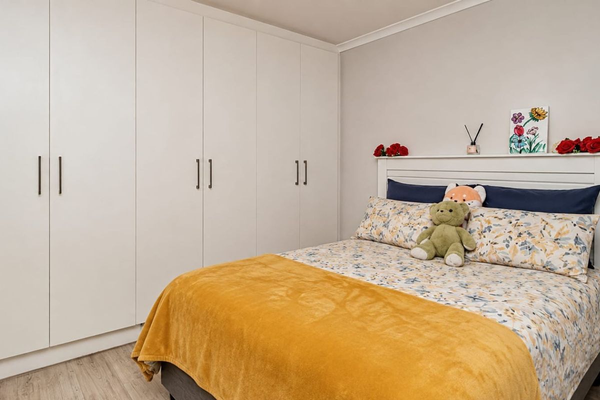 A well-maintained bedroom featuring extensive floor-to-ceiling built-in cupboards and light-toned laminate flooring.