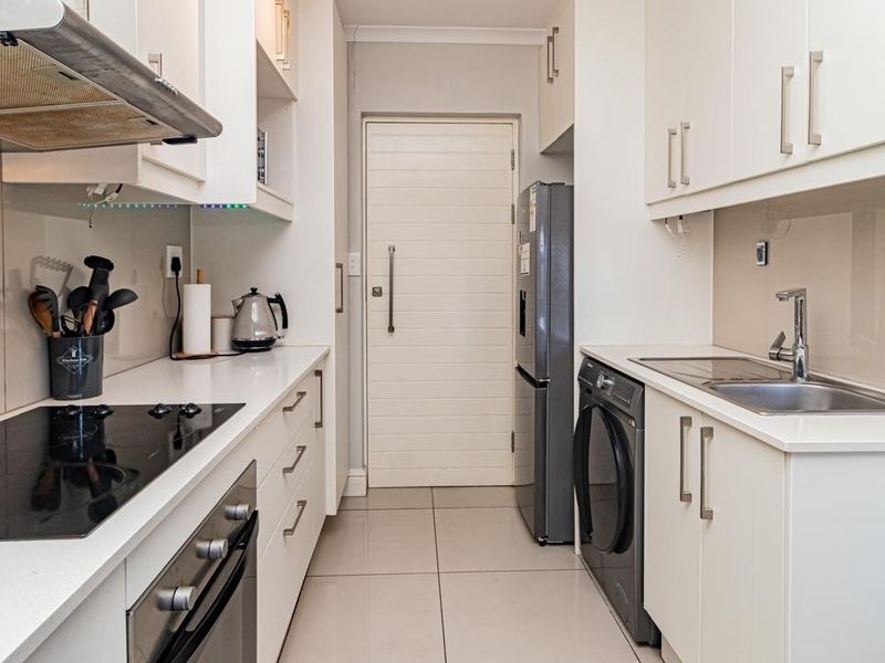 A modern, compact kitchen featuring white cabinetry, stone countertops, integrated appliances, and tiled flooring, offering a clean and functional workspace.