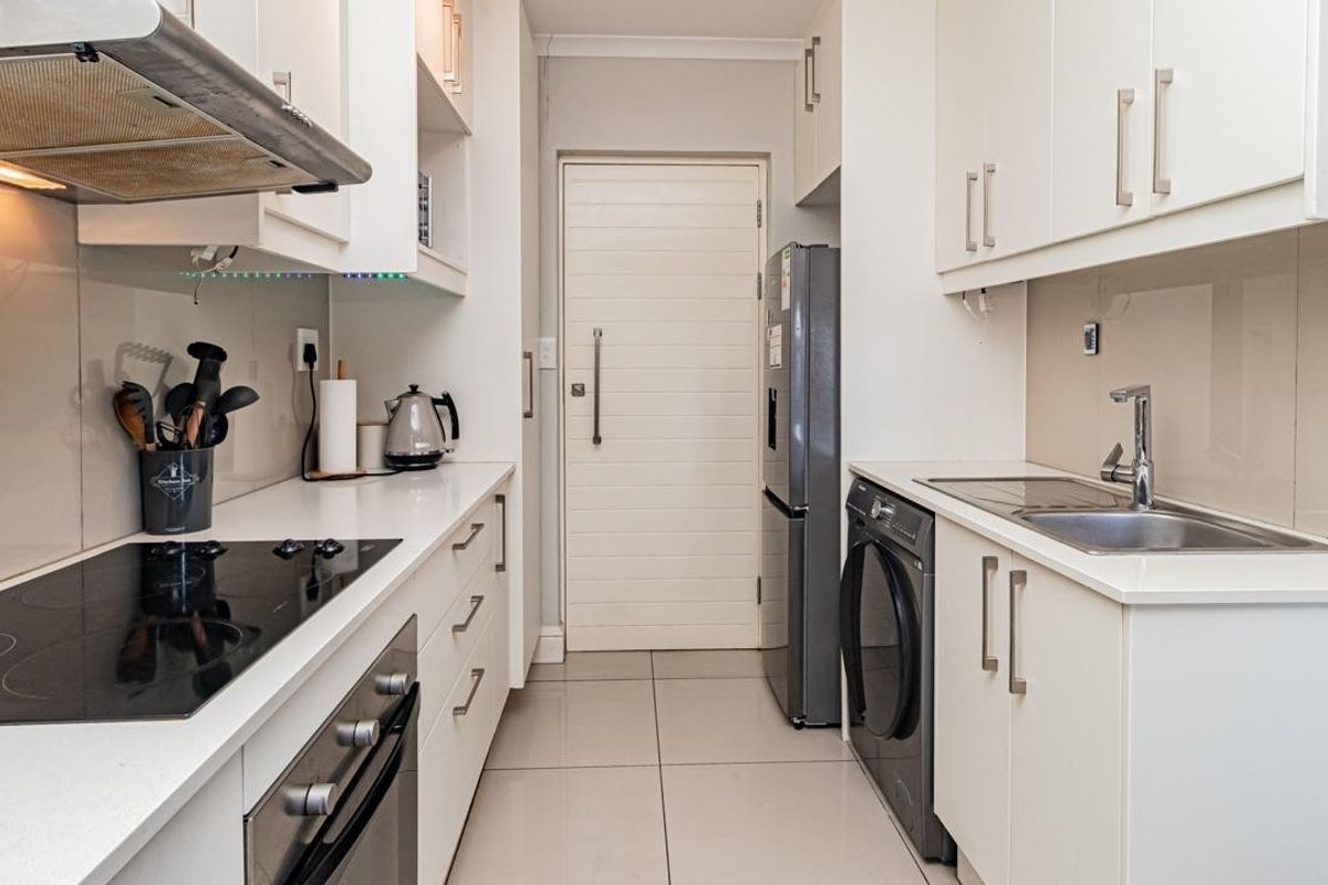 A modern, compact kitchen featuring white cabinetry, stone countertops, integrated appliances, and tiled flooring, offering a clean and functional workspace.