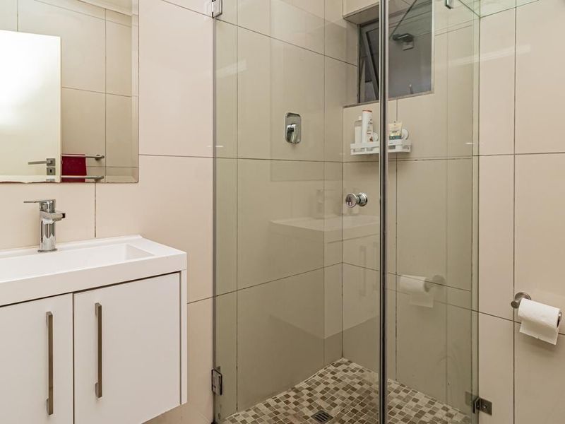 Modern bathroom featuring a sleek vanity cabinet, wall-mounted mirror, and a glass-enclosed shower with neutral tiled finishes.