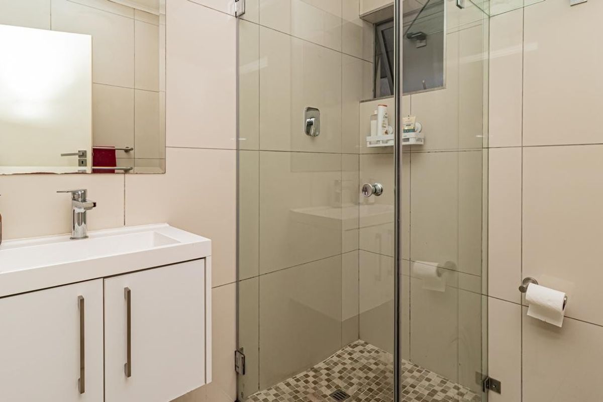 Modern bathroom featuring a sleek vanity cabinet, wall-mounted mirror, and a glass-enclosed shower with neutral tiled finishes.