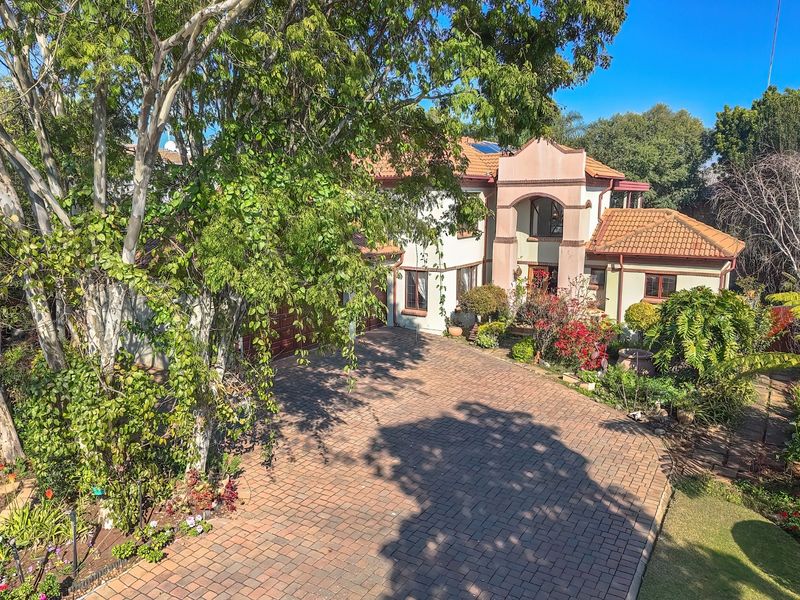 Elevated view of the front facade featuring a paved driveway, double garage, and a prominent covered entrance portico with established garden landscaping.