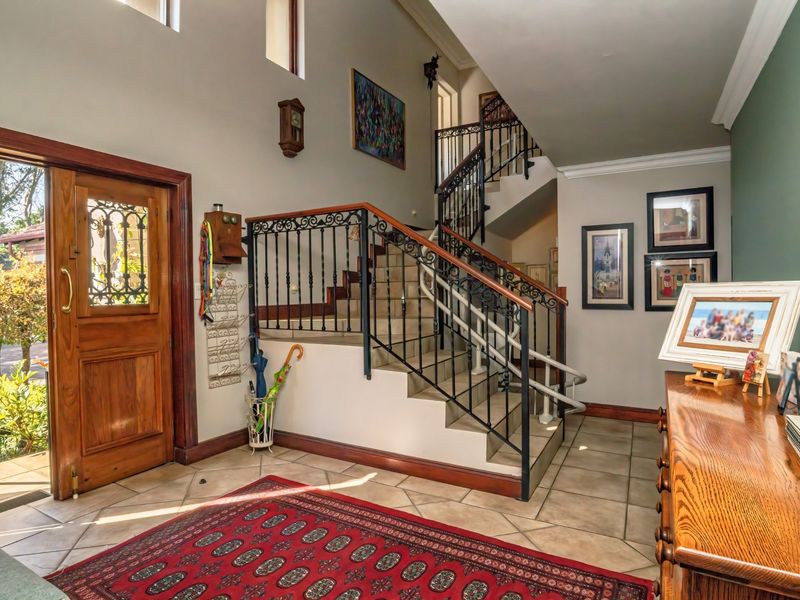 Spacious double-volume entrance hall featuring tiled flooring, a grand staircase with wrought iron balustrades, and a solid wooden front door.
