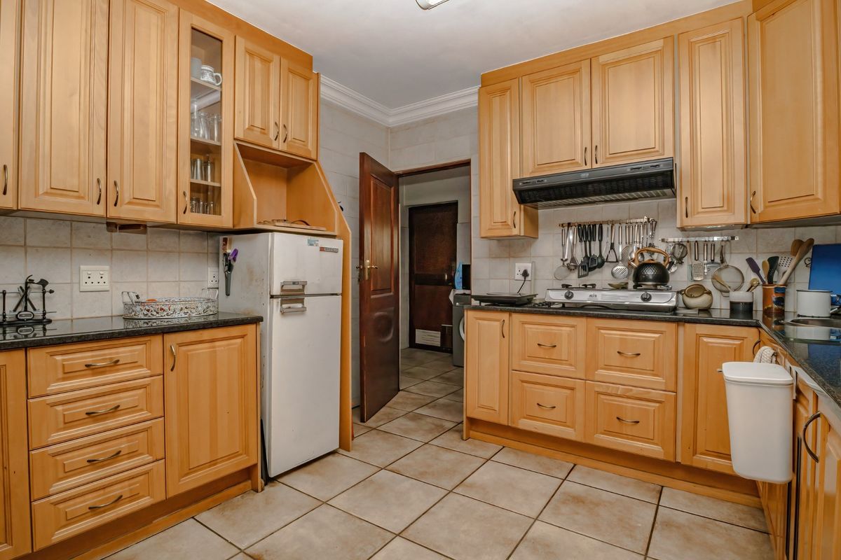 A functional kitchen featuring wooden cabinetry, granite countertops, a gas hob with extractor fan, and tiled flooring throughout.