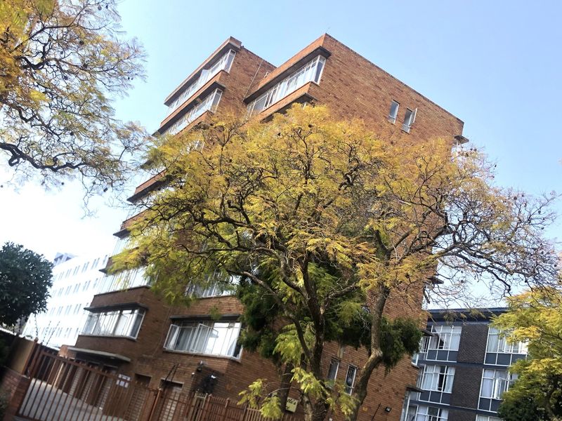 A multi-story brick apartment building featuring large casement windows and a secure metal gated entrance.