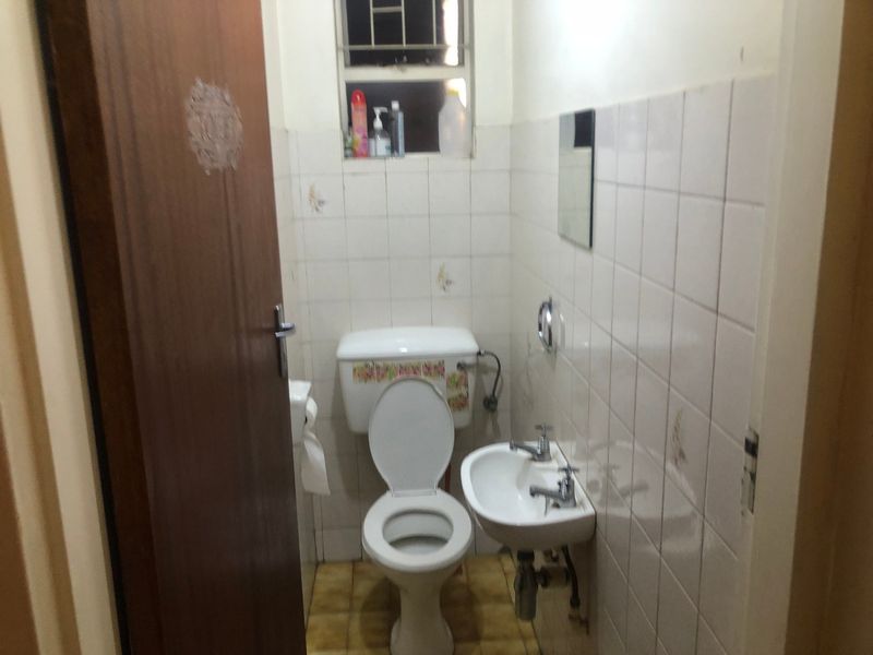 A compact bathroom featuring a standard toilet, wall-mounted basin, and tiled finishes, requiring modernization to improve its overall condition and aesthetic appeal.