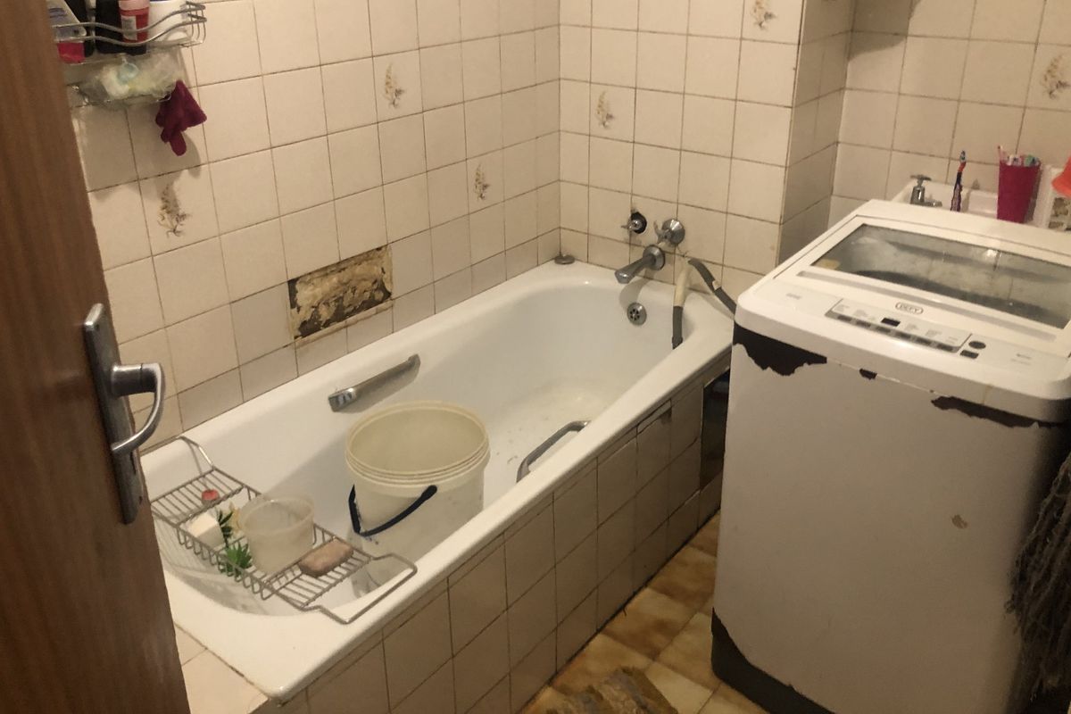 A dated bathroom featuring a bathtub with wall tiling and floor tiles, currently showing signs of wear and missing wall tiles requiring repair.