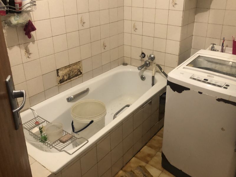 A dated bathroom featuring a bathtub with wall tiling and floor tiles, currently showing signs of wear and missing wall tiles requiring repair.