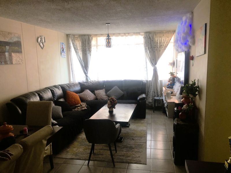 A living room area featuring tiled flooring and a textured ceiling, with natural light entering through a large window.