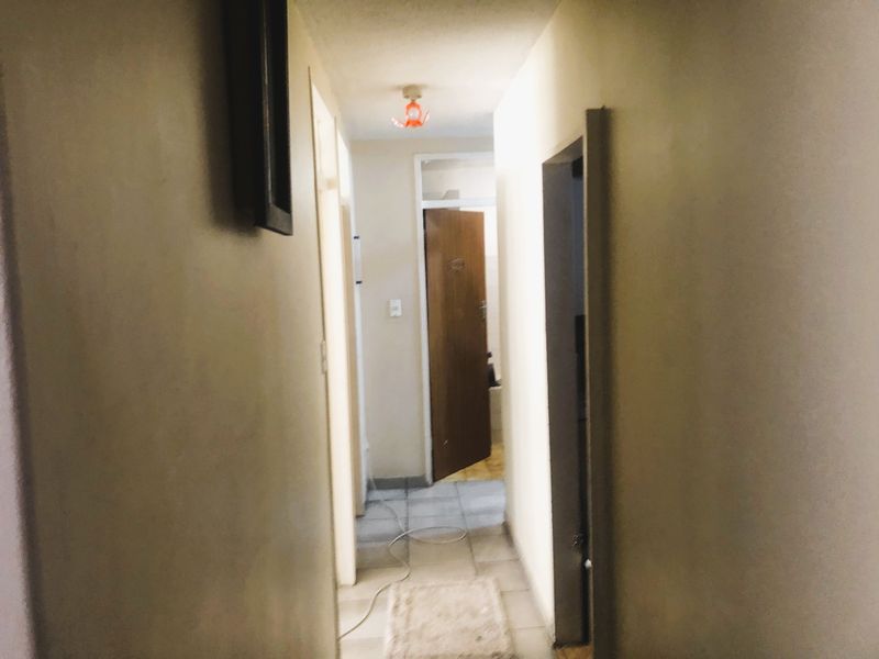 A narrow residential hallway featuring tiled flooring and access to multiple rooms, requiring cosmetic updates to improve the overall aesthetic.