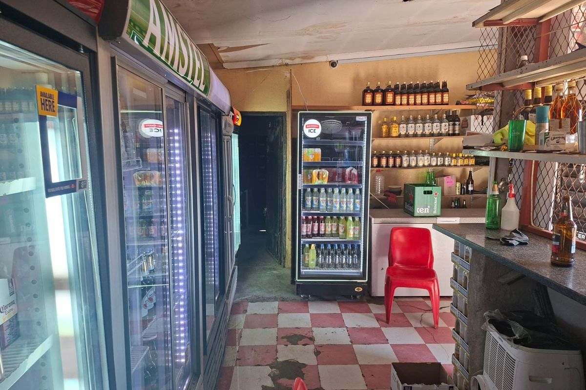 Commercial bar area featuring built-in shelving, service counter, and tiled flooring, currently showing significant signs of wear and ceiling damage.