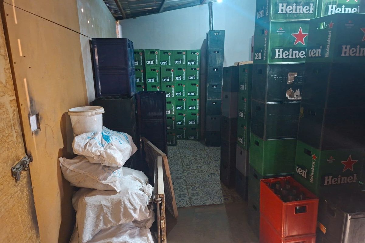 A utility storage area featuring patterned floor tiles and exposed roof structure, currently used for bulk storage of beverage crates.