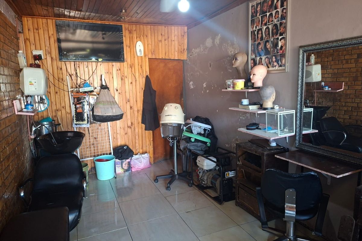 A commercial salon space featuring timber ceiling paneling, ceramic floor tiles, and exposed brick walls, currently equipped with salon infrastructure and workstations.