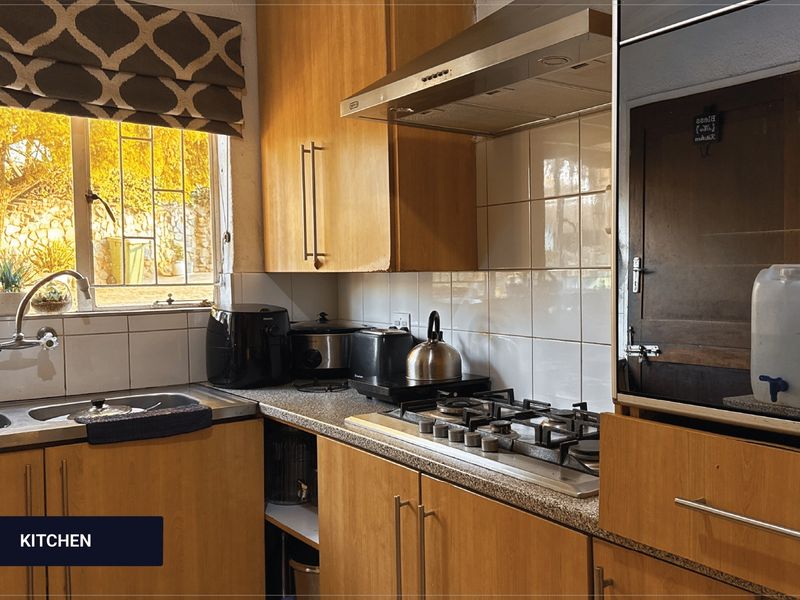 A functional kitchen featuring wooden cabinetry, a gas hob with extractor fan, tiled backsplash, and a stainless steel sink overlooking the garden.