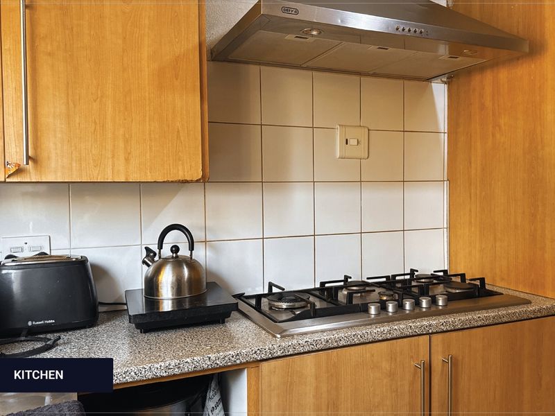 A functional kitchen area featuring wooden cabinetry, granite countertops, a gas hob, and a stainless steel extractor fan with tiled backsplash.