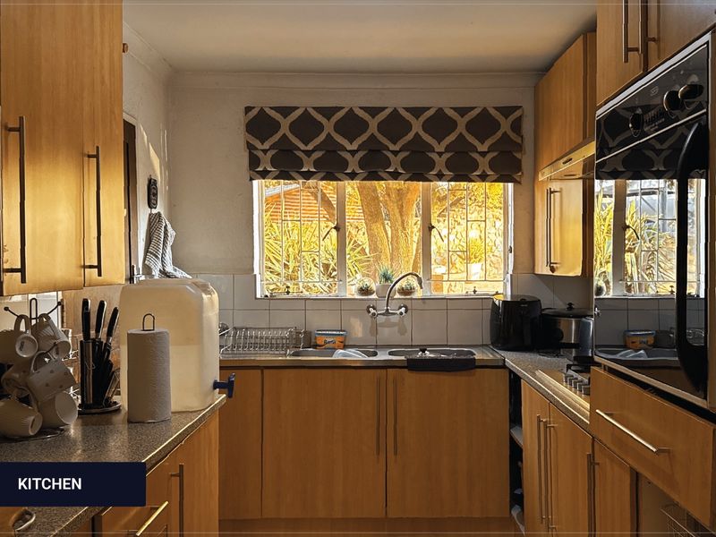 A functional kitchen featuring built-in wooden cabinetry, laminate countertops, a stainless steel double sink, and a built-in oven with a tiled backsplash.