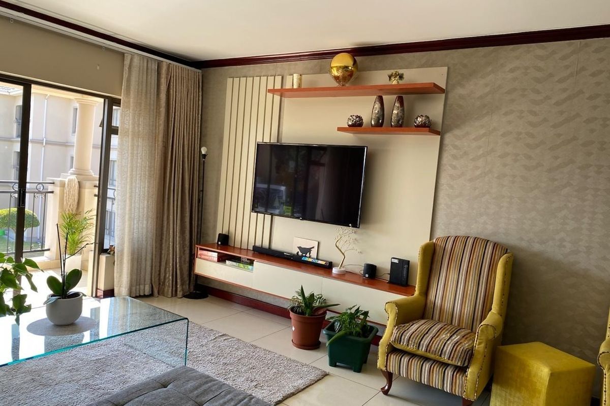 A well-maintained living room featuring a custom built-in media unit with floating shelves, tiled flooring, and direct access to a balcony through sliding doors.