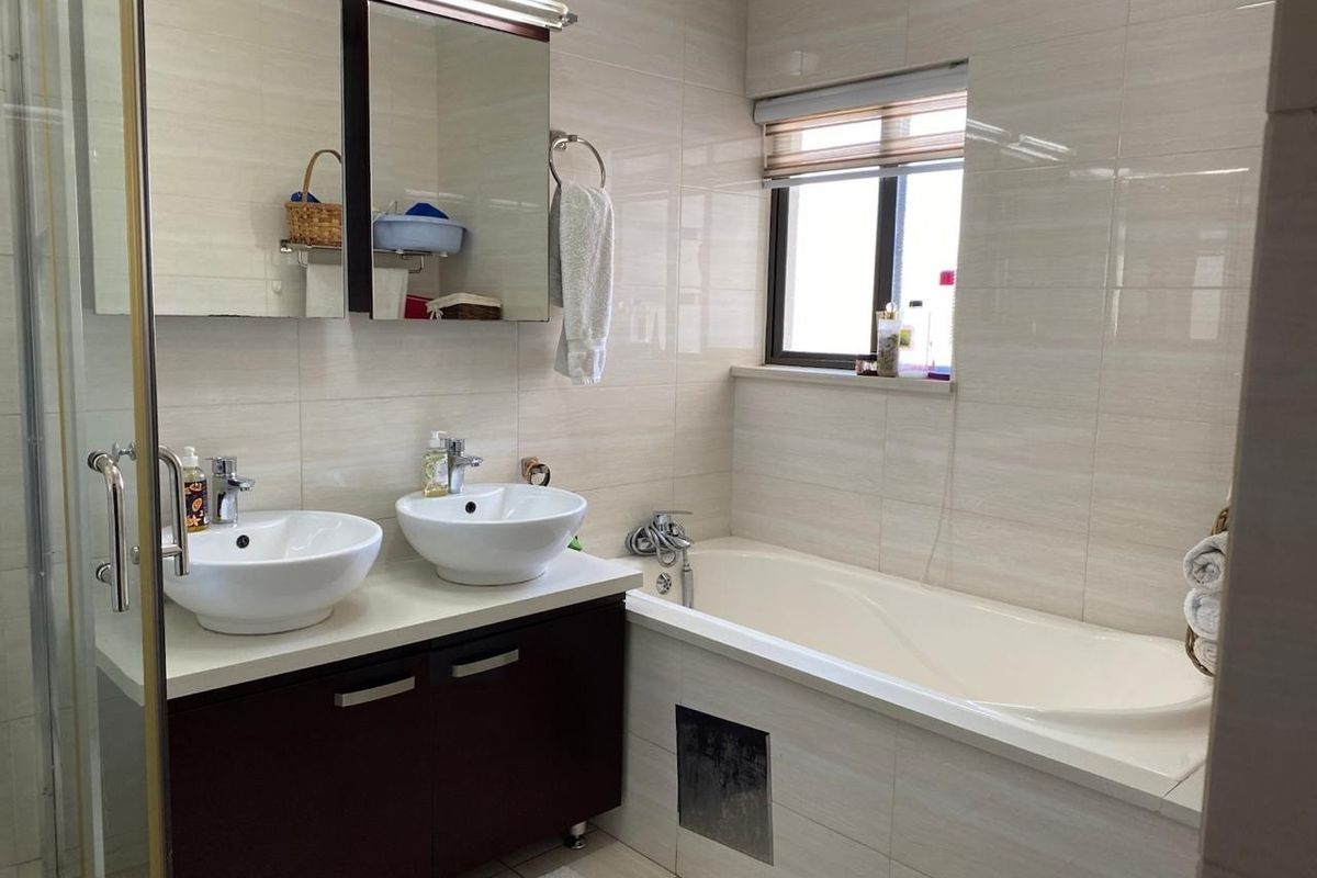 A functional bathroom featuring a double vanity with vessel sinks, a built-in bathtub, and a separate shower enclosure with neutral wall tiling.