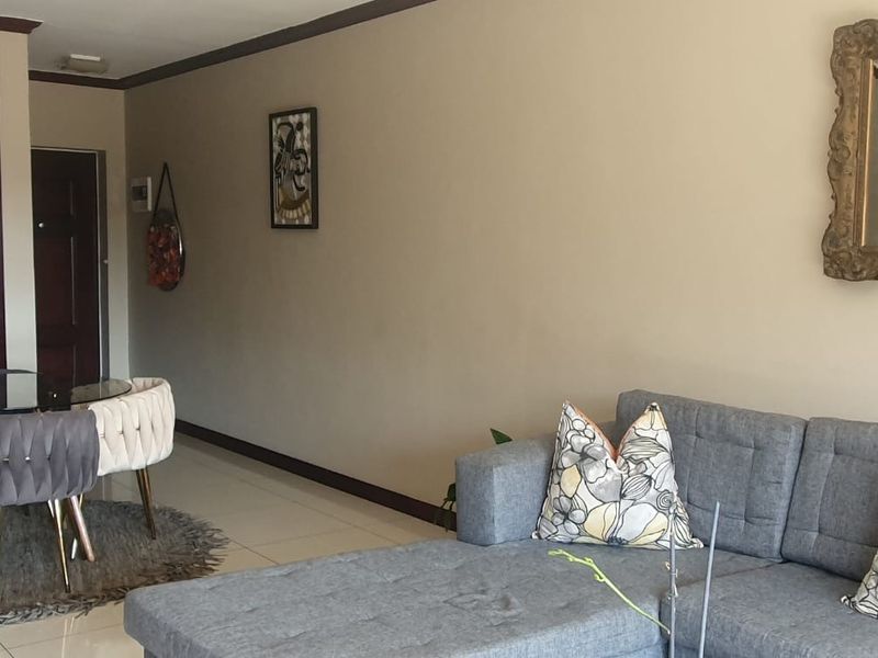 An open-plan living and dining area featuring tiled flooring, crown molding, and a connected kitchen with built-in cabinetry and a wine rack.