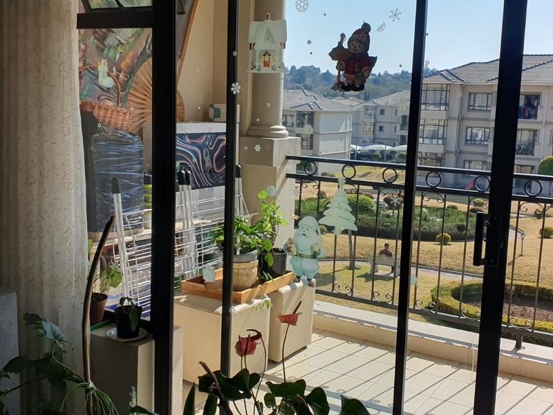 A balcony featuring tiled flooring and a wrought iron railing, offering views of the apartment complex grounds.