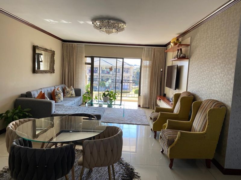 A well-maintained living room featuring polished porcelain tiles, crown molding, a crystal chandelier, and large sliding glass doors leading to a balcony.
