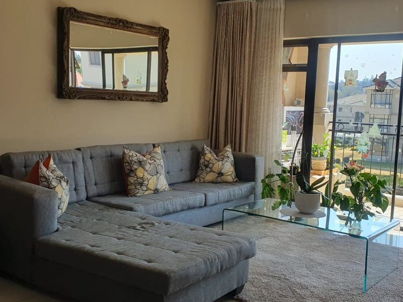 A comfortable living room featuring tiled flooring and a large sliding glass door that opens onto a balcony with views of the complex.