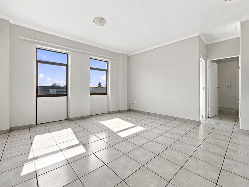 Bright and spacious open-plan living area featuring neutral tiled flooring, large windows for natural light, and a compact integrated kitchen.