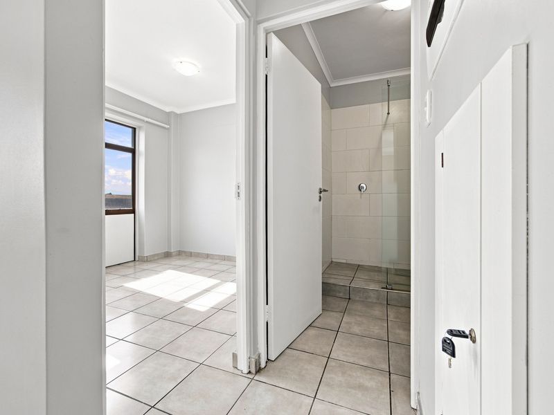 A bright hallway leading to an adjacent bedroom and a tiled shower room with neutral finishes.