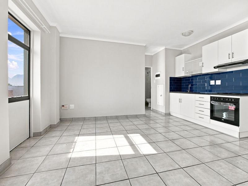 Bright open-plan living area featuring tiled floors and a modern kitchen with white cabinetry, built-in oven, extractor fan, and a striking blue tile backsplash.