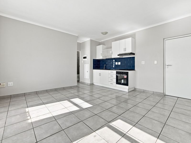 An open-plan living and kitchen area featuring neutral tiled flooring, white cabinetry, a dark subway tile backsplash, and integrated cooking appliances.