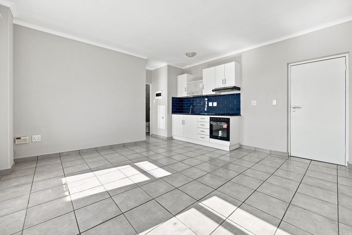 An open-plan living and kitchen area featuring neutral tiled flooring, white cabinetry, a dark subway tile backsplash, and integrated cooking appliances.