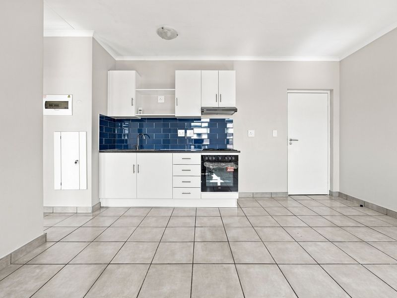 A clean, modern kitchen featuring white cabinetry, a striking blue subway tile backsplash, integrated oven, and neutral ceramic floor tiles in an open-plan layout.