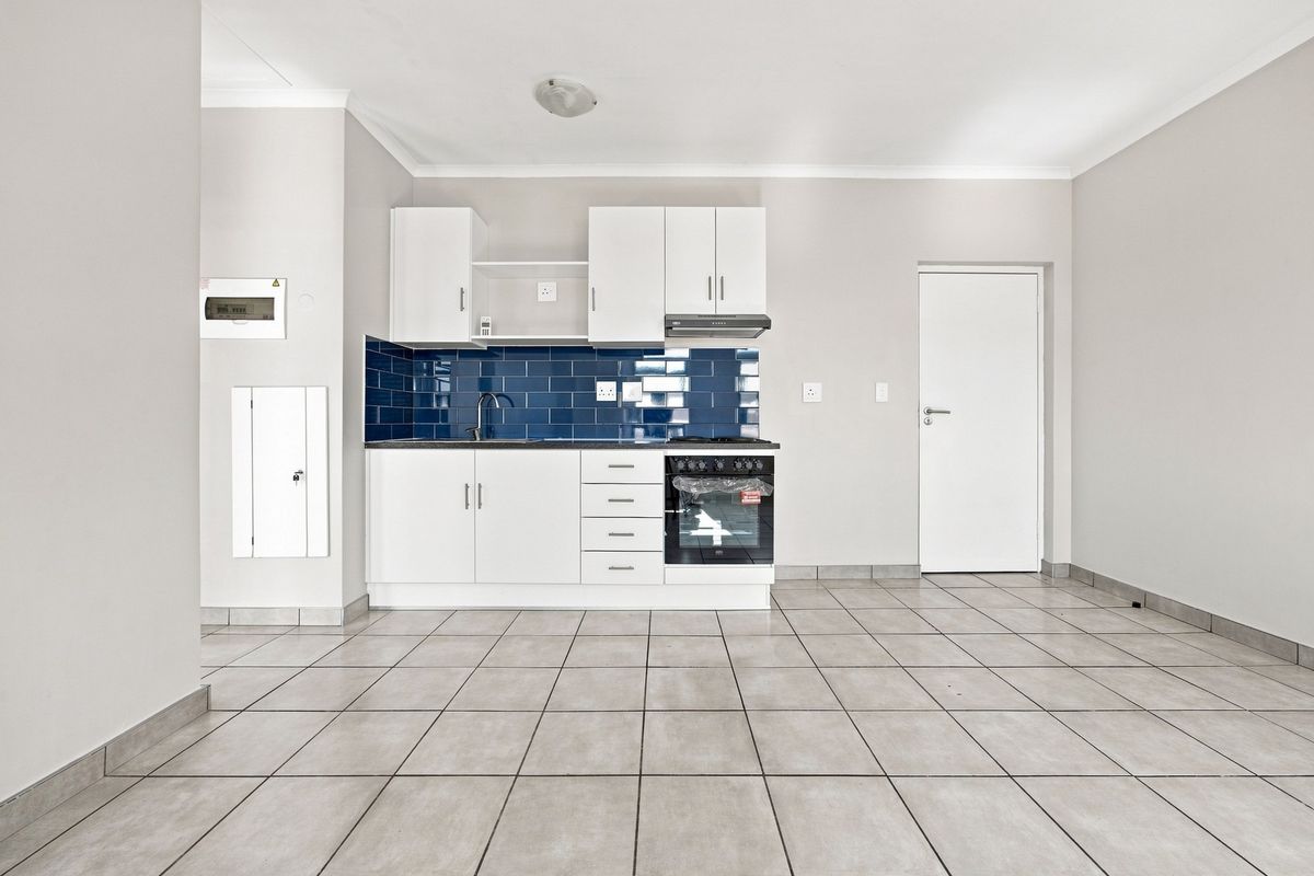 A clean, modern kitchen featuring white cabinetry, a striking blue subway tile backsplash, integrated oven, and neutral ceramic floor tiles in an open-plan layout.