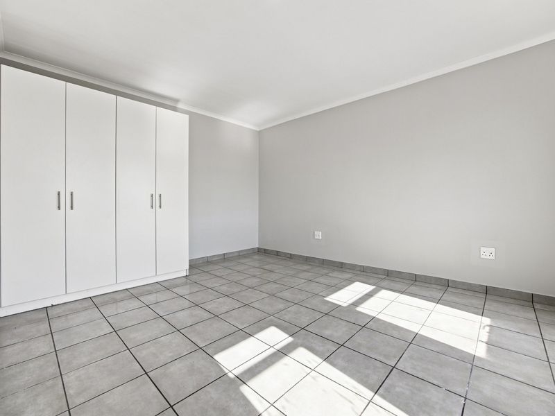 A bright, empty bedroom featuring neutral grey tiled flooring, clean white walls, and ample built-in cupboard storage.