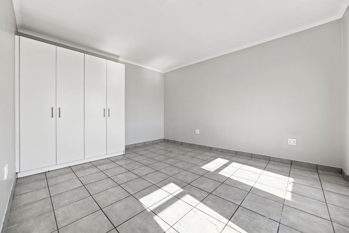 A bright, empty bedroom featuring neutral grey tiled flooring, clean white walls, and ample built-in cupboard storage.
