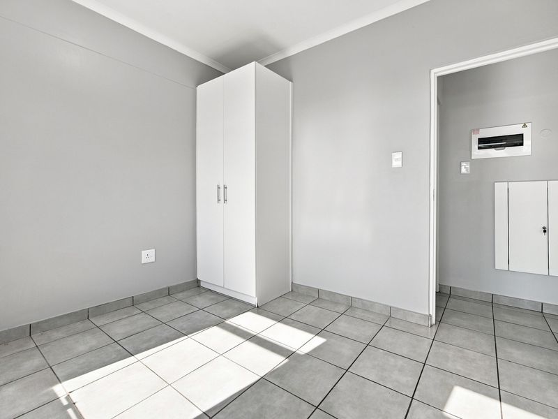 A clean, empty bedroom featuring neutral grey walls, durable tiled flooring, and a built-in wardrobe, offering a versatile space ready for personalization.
