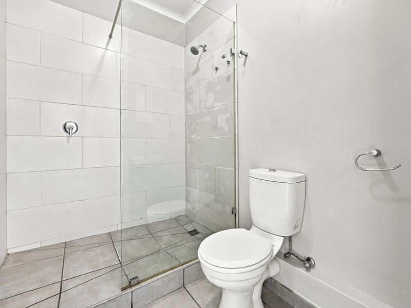 A bathroom featuring a walk-in shower with a glass screen and a standard toilet, currently requiring completion of the wall tiling.