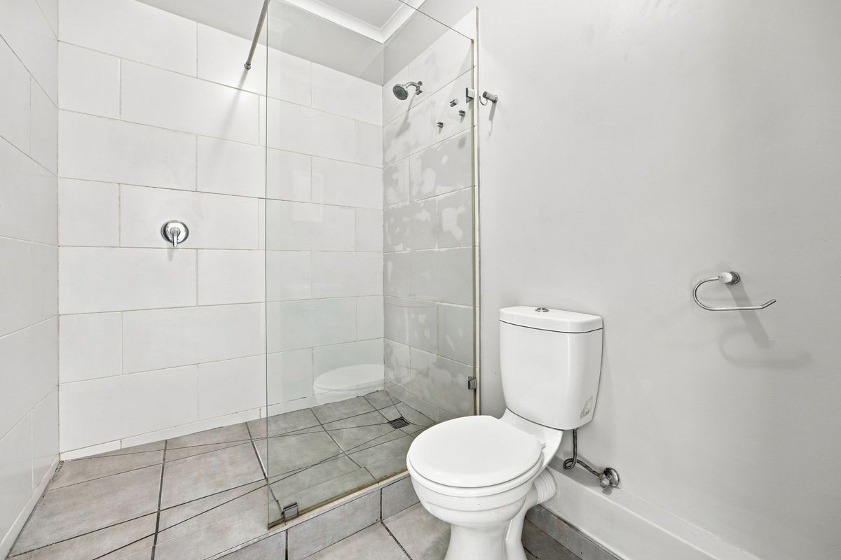 A bathroom featuring a walk-in shower with a glass screen and a standard toilet, currently requiring completion of the wall tiling.