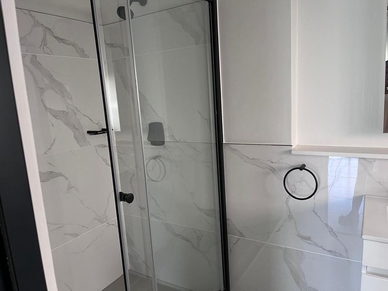 Modern bathroom featuring a walk-in shower with a black frame, marble-look wall tiles, and a sleek vanity unit.