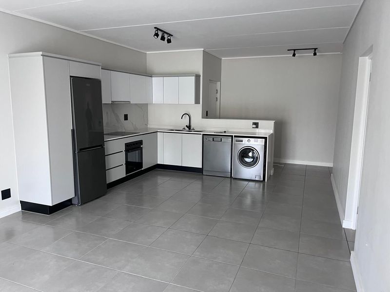 Modern open-plan kitchen featuring sleek white cabinetry, stone countertops, integrated appliances, and neutral tiled flooring in a clean, well-maintained space.