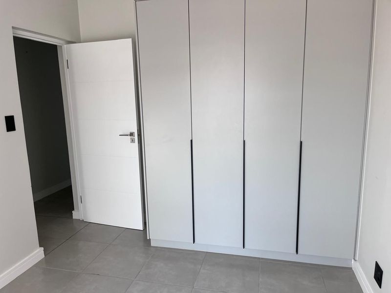A clean, modern bedroom featuring neutral tiled flooring and floor-to-ceiling built-in wardrobes with sleek black handles.