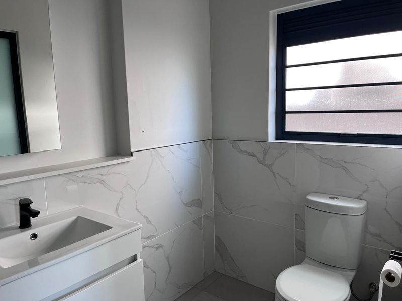 Modern bathroom featuring marble-look wall tiles, a sleek vanity with a black mixer tap, and a window with security bars.