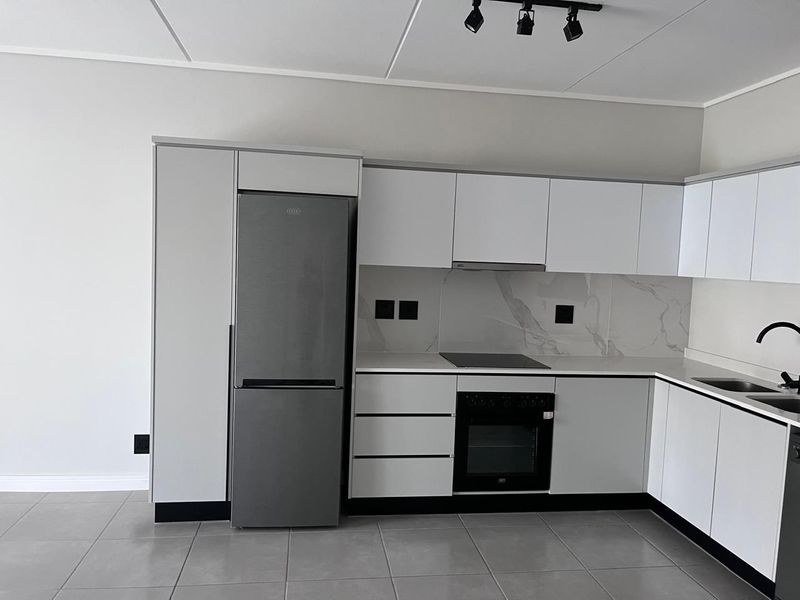 Modern kitchen featuring white cabinetry, stone countertops, marble-look splashback, integrated appliances, and sleek track lighting in a clean, contemporary finish.