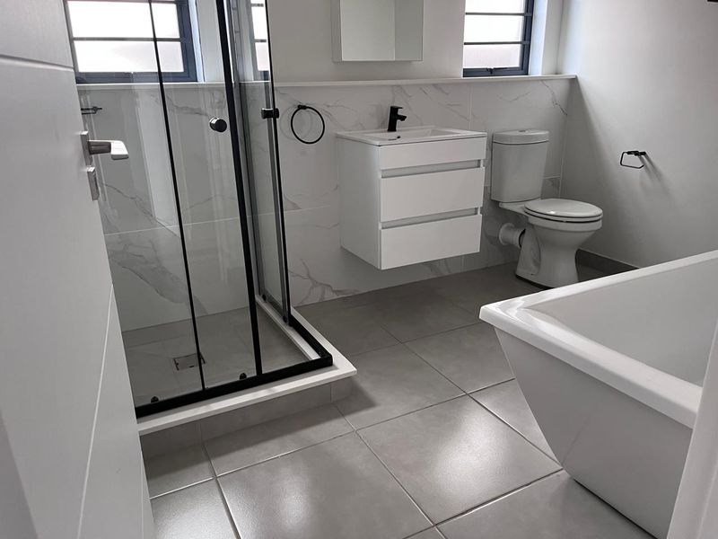 Modern bathroom featuring a walk-in shower with black frame, wall-mounted vanity, freestanding bathtub, and contemporary marble-look wall tiling.