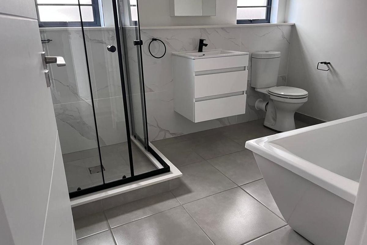 Modern bathroom featuring a walk-in shower with black frame, wall-mounted vanity, freestanding bathtub, and contemporary marble-look wall tiling.
