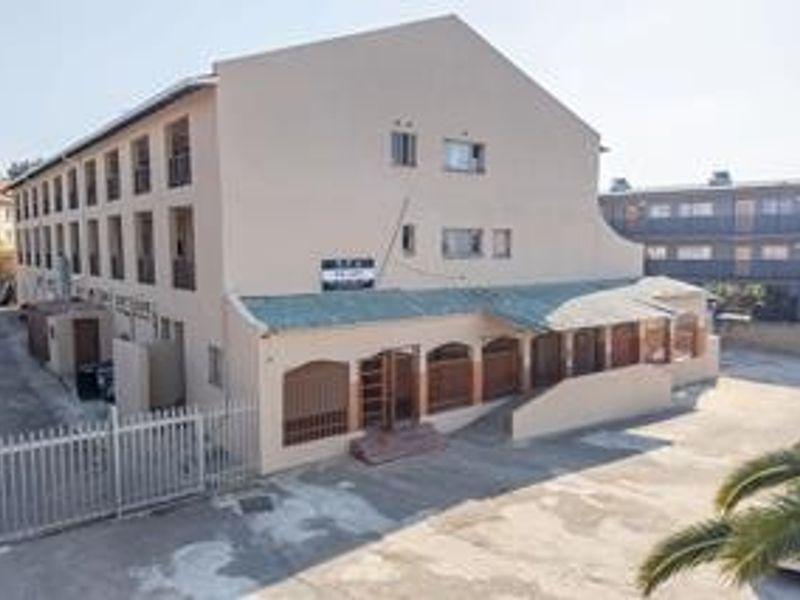A multi-story commercial building featuring a paved driveway, security fencing, and a covered entrance area.