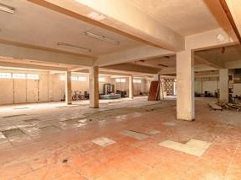A large, open-plan commercial utility space featuring concrete columns, tiled flooring, and industrial-style fluorescent lighting, suitable for storage or workshop use.