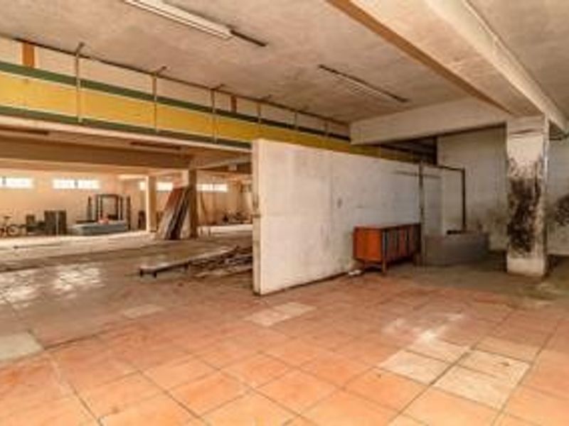 Large open-plan commercial space featuring tiled flooring, exposed concrete ceilings, and structural columns, requiring significant refurbishment and cosmetic updates.